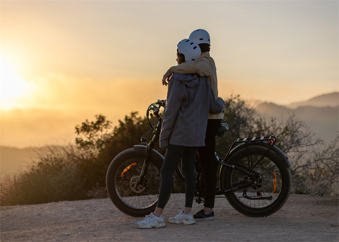 Two people in helmets embracing beside a TESWAY S7 electric bike against a sunset backdrop